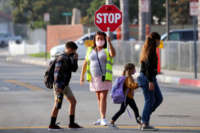 A crossing guard help cross the street as students return, after months of closure due COVID-19 pandemic, at James H. Cox Elementary School on September 23, 2020 in Fountain Valley, California.