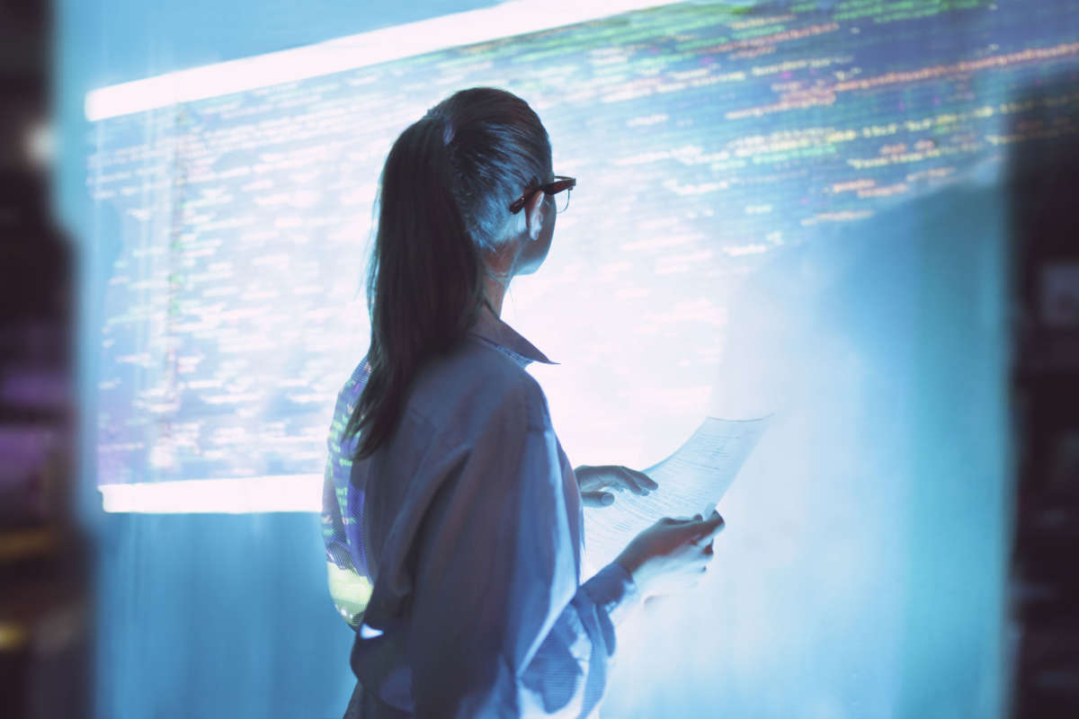 A woman reviews computer code projected on a wall