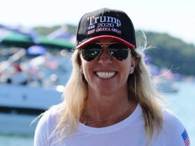 Marjorie Taylor Greene wearing a Trump hat in front of boats