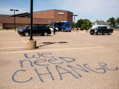 "WE NEED CHANGE" is spraypainted on the concrete of a U.S. Bank parking lot