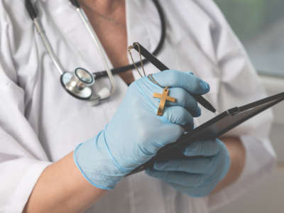 A doctor writes on a tablet, a cross attached to her pen.