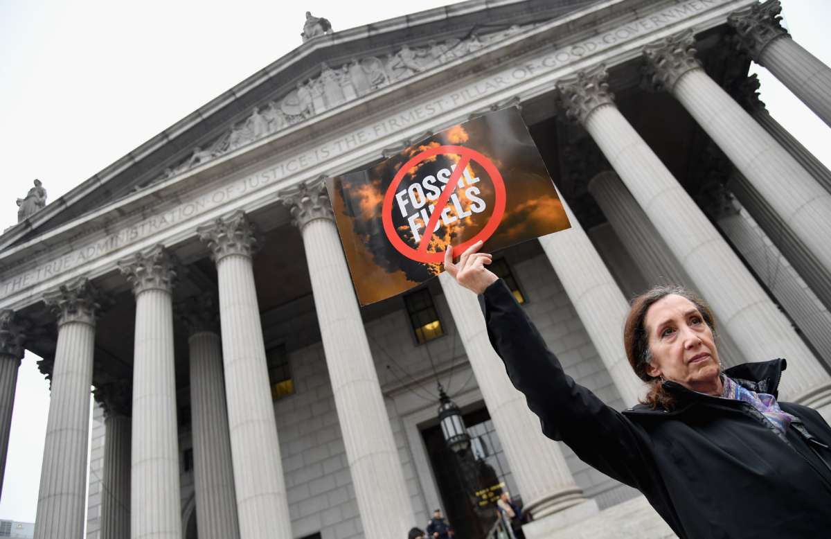 a woman holds a sign reading "[no] FOSSIL FUELS" in front of the new york supreme court building