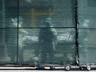 Hospital personnel behind a barricade move deceased individuals to the overflow morgue trailer outside The Brooklyn Hospital Center on May 7, 2020, in the Brooklyn borough of New York City.