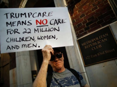 A protester holds a sign reading "TRUMPCARE MEANS NO CARE FOR 22 MILLION CHILDREN, WOMEN AND MEN" during a pre-covid protest
