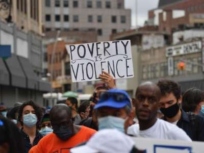 A protester holds a sign reading "POVERTY IS VIOLENCE" during an outdoor rally