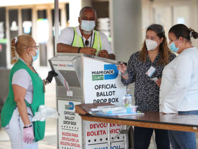 Poll workers help a voter put their mail-in ballot in an official Miami-Dade County ballot drop box on August 11, 2020, in Miami, Florida.