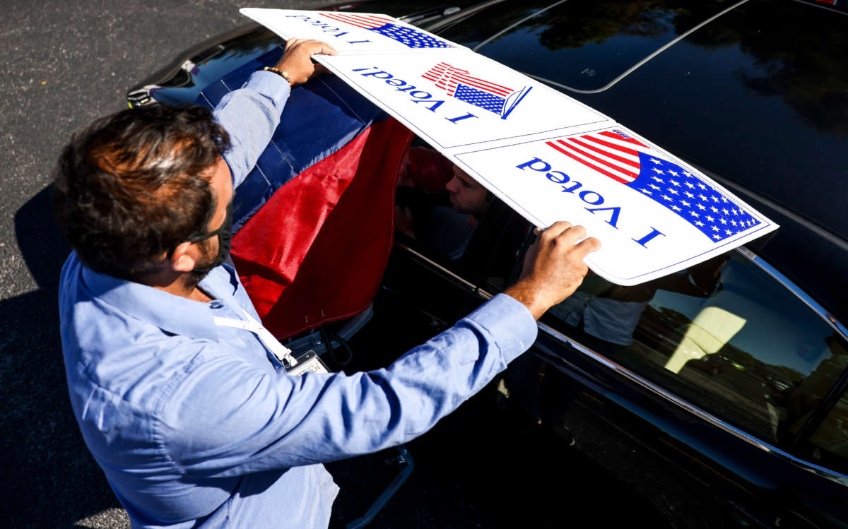 A poll worker shields the voting screen as a man votes from his car during curbside voting at Seacoast Church West Ashley on October 30, 2020, in Charleston, South Carolina.