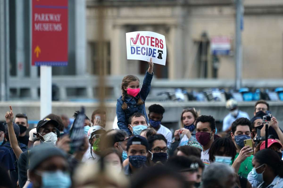 A girl holds a sign reading "VOTERS DECIDE" while sitting on her dad's shoulders during a protest