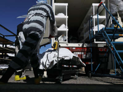Inmates from El Paso County detention facility load bodies wrapped in plastic into a refrigerated temporary morgue trailer in a parking lot of the El Paso County Medical Examiner's office on November 16, 2020, in El Paso, Texas.