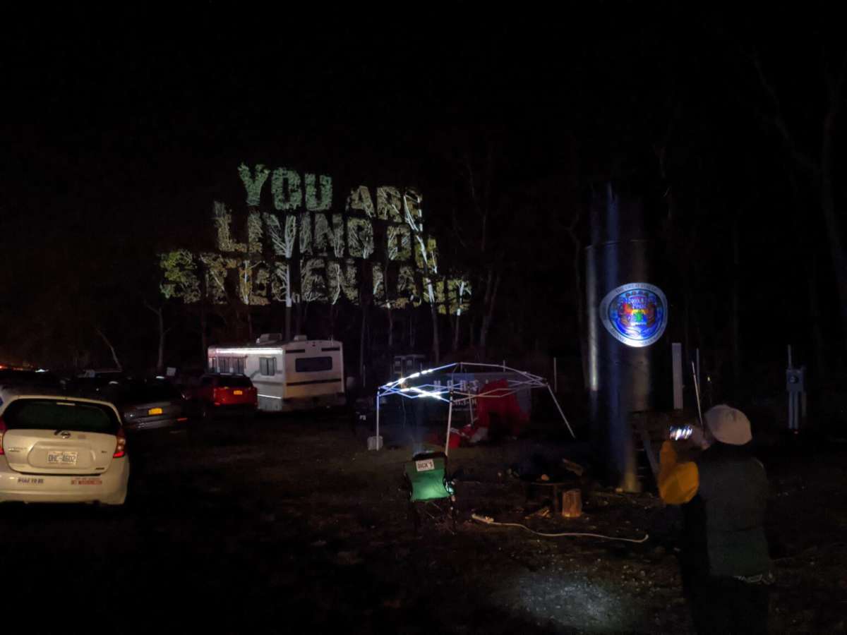 “You are living on stolen land” projected on trees over Sovereignty Camp that drivers can see before entering the Shinnecock Hills.