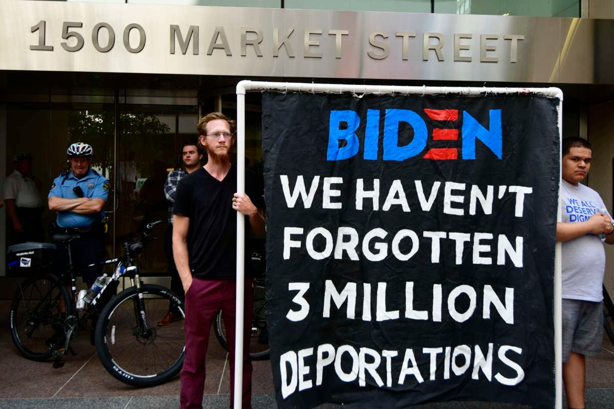 Two activists display a banner reading "BIDEN: WE HAVEN'T FORGOTTEN 3 MILLION DEPORTATIONS"
