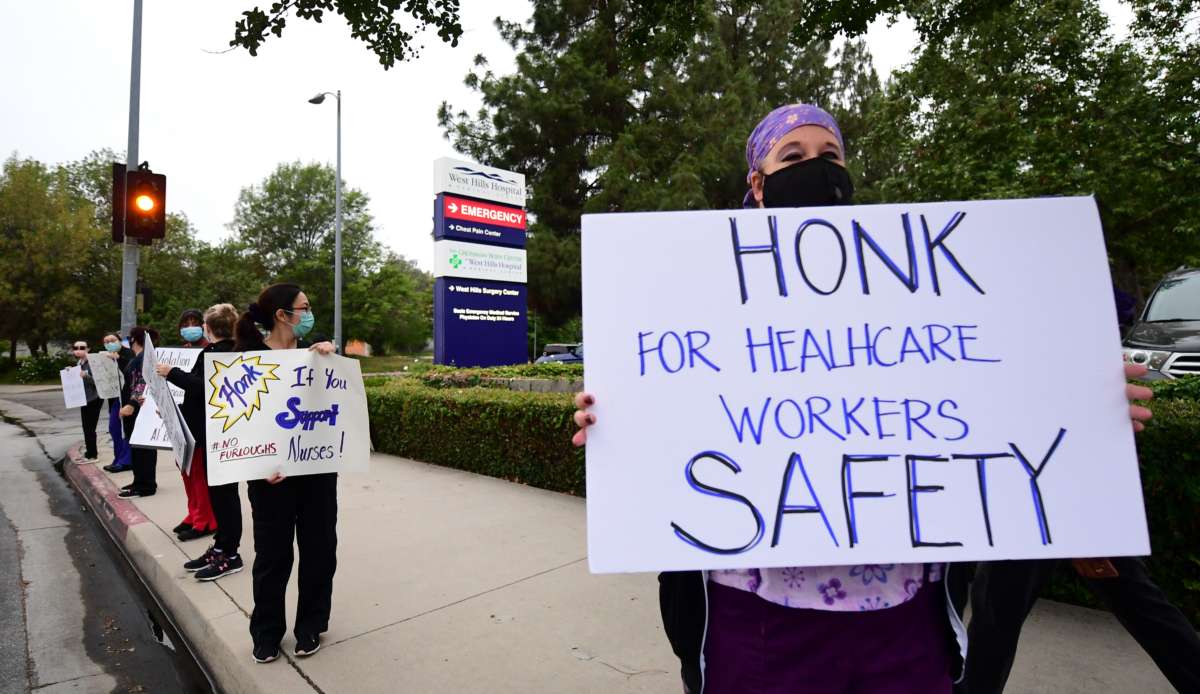 A masked nurse holds a sign reading "HONK IF YOU SUPPORT NURSES" during a curbside covid-era protest