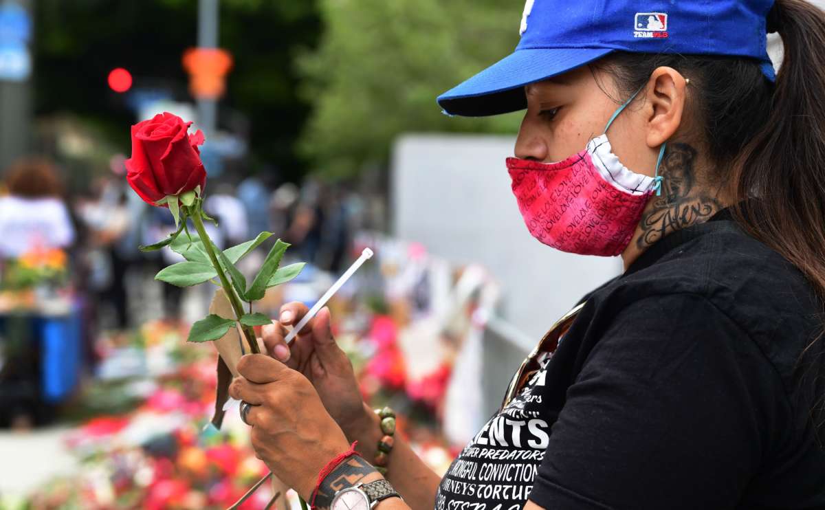 A masked woman holds a rose near a memorial