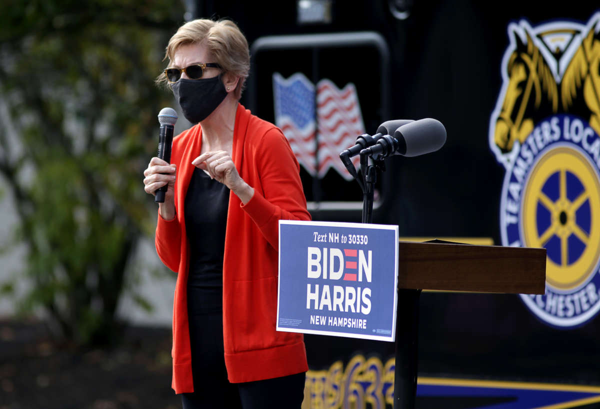 A masked Elizabeth Warrenspeaks while standing on a podium