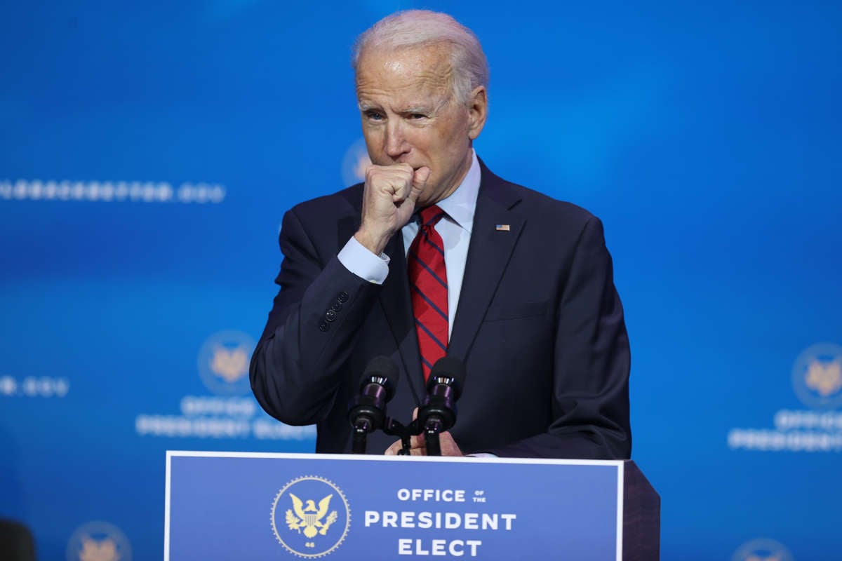An unmasked President Elect Joseph R. Biden coughs into his hand in the age of covid