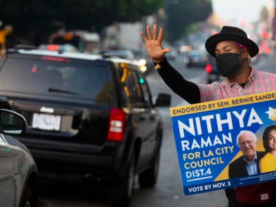 As the sun begins to set, Matthew Gaston of Los Angeles holds up a vote sign for Nithya Raman for LA City Council down the street from a voting center inside The Wiltern on election day on November 3, 2020, in Los Angeles, CA.