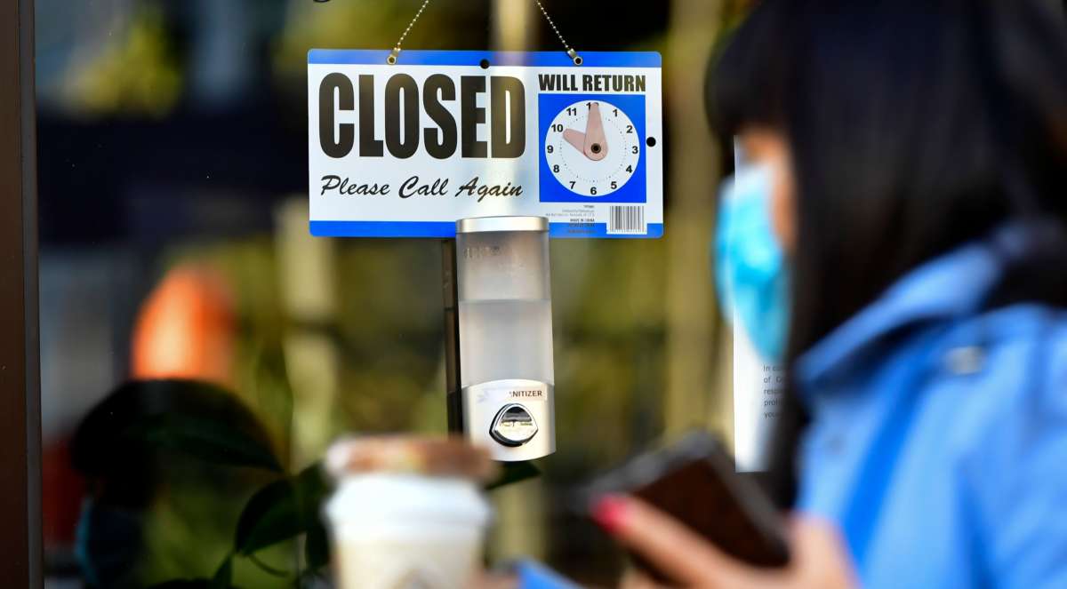 A pedestrian wearing her facemask and holding a cup of coffee walks past a closed sign hanging on the door of a small business in Los Angeles, California, on November 30, 2020.