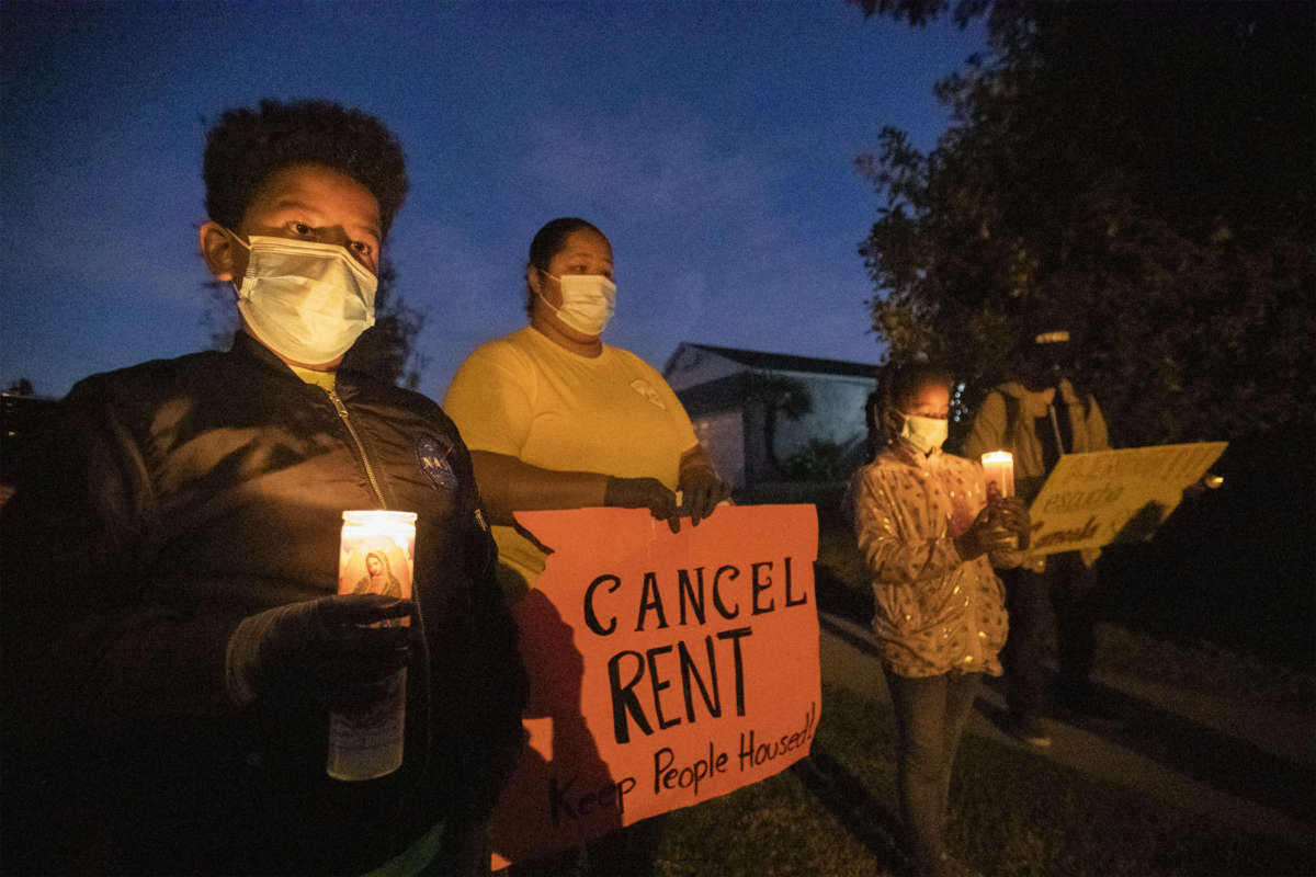 Masked people hold signs during a candlelight vigil decrying evictions