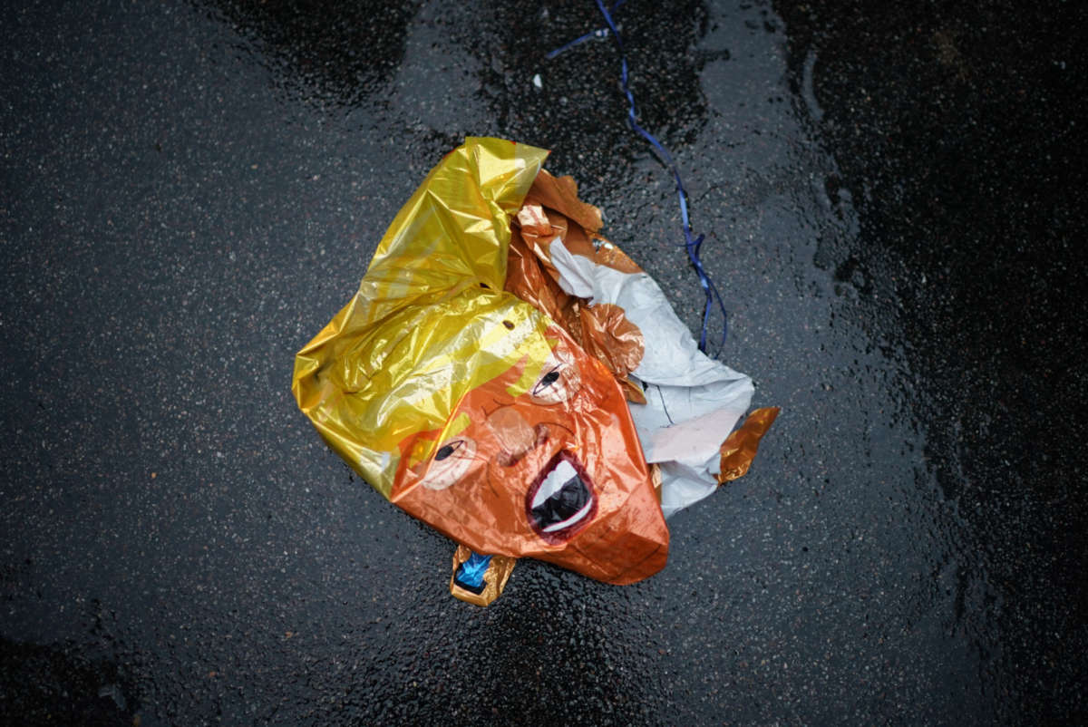 A popped trump balloon lies deflated on the wet asphalt