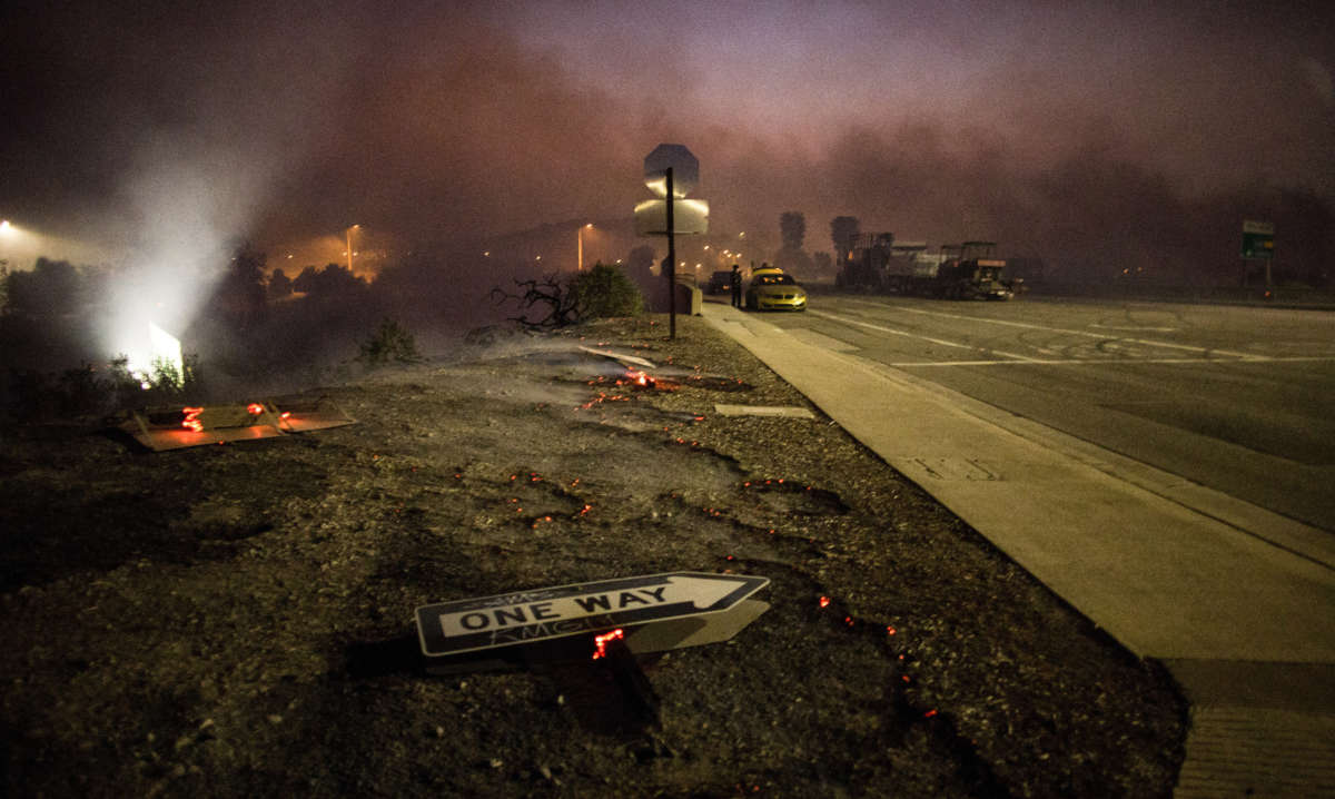 A "One Way" street sign lies on burnt ground as a brush fire surrounds it in Irvine, California, on October 26, 2020.