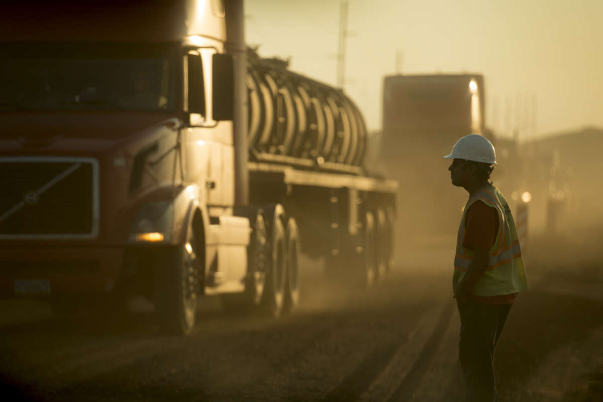 A worker in construction gear watches oil trucks drive by