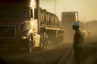 A worker in construction gear watches oil trucks drive by