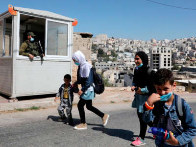 Palestinian children pass in front of an Israeli checkpoint as they walk to their house in Al-Shuhada Street, which is largely closed to Palestinians, in the city center of the West Bank town of Hebron, on September 24, 2020.