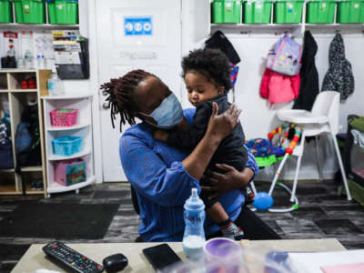 Kiddies Corner daycare owner Anne Osula holds a child before putting him down for a nap at the daycare in Boston's Mattapan on February 12, 2021.