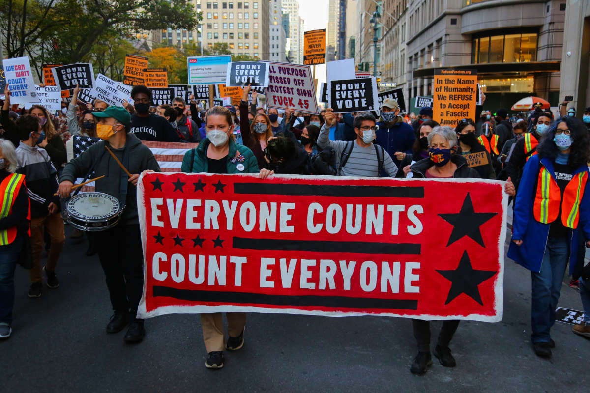 Activists march behind a banner reading "EVERYONE COUNTS, COUNT EVERYONE" during a street protest