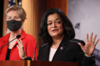 Pramila Jayapal speaks at a podium as Elizabeth Warren stands in the background