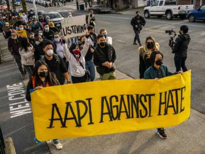 People march behind a banner reading "AAPI AGAINST HATE" during a protest
