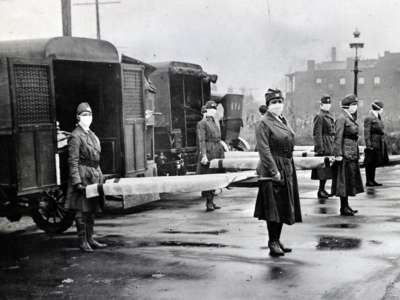 St. Louis Red Cross Motor Corps on duty during the Spanish Influenza epidemic, 1918. Photograph shows mask-wearing woman holding stretchers at backs of ambulances.