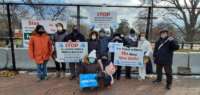 People stand in front of a fence holding signs decrying military exercises in Korea