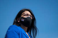 A masked Rashida Tlaib wears blue against a blue sky