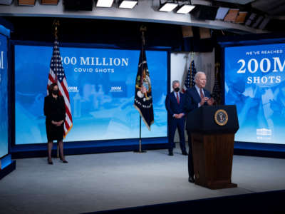 Joe Biden speaks in front of displays that read "WE'VE REACHED 200 MILLION SHOTS"