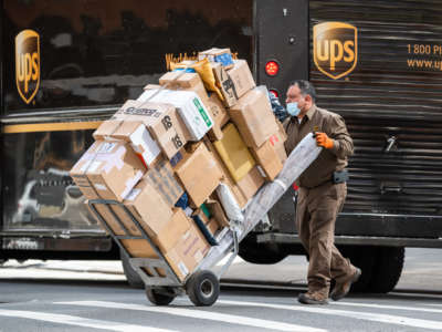 A UPS worker wheels a bunch of boxes across a street