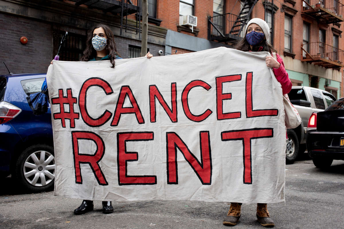Two masked activists hold a banner reading "CANCEL RENT"