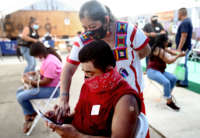 An elder helps a man with a bandaid on his forearm navigate something on his phone