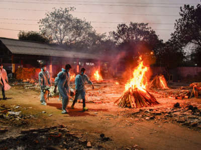 Workers carry the body of a person who has died from COVID-19 as other funeral pyres are seen burning during a mass cremation held at a crematorium in New Delhi, India, on May 3, 2021.
