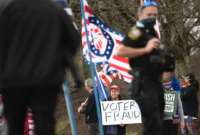 a man holds a sign reading "VOTER FRAUD" at a rally