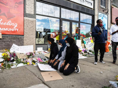 Three young Muslim women pray at the site of George Floyd's murder