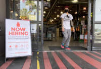 A man exits a store with a "NOW HIRING" sign in front of it