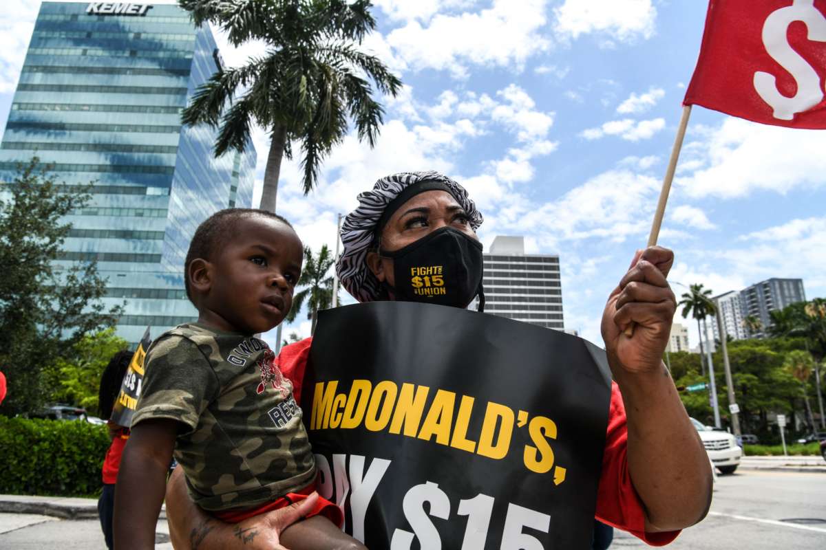 A masked woman holds both her grandbaby and a sign demanding higher wages during a protest