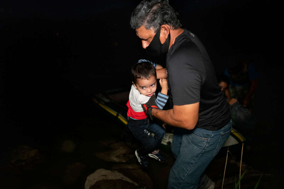 A masked man pulls a toddler out of a raft in the dark
