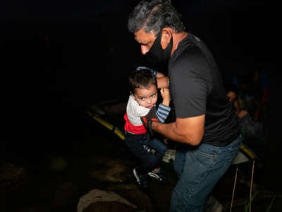 A masked man pulls a toddler out of a raft in the dark