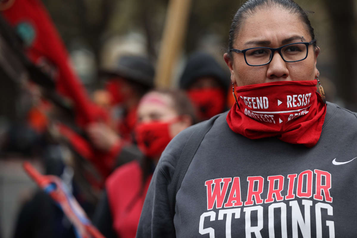 An Indigenous activist with perfect eyebrows looks onward as other activists demonstrate behind her