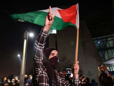 A demonstrator raises a hand with the victory gesture while holding a Palestinian flag outside the Haifa District Court in Israel's northern Mediterranean coastal city on February 27, 2021, during a protest by Arab Israelis in solidarity with Palestinians.