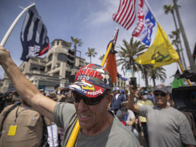 An Evangelical Christian Donald Trump supporter carries flags at the site of a "White Lives Matter" rally on April 11, 2021, in Huntington Beach, California.