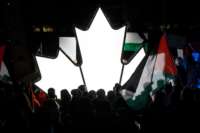 People stand near an illuminated Canadian Maple leaf as thousands gather in Toronto, Ontario, Canada to show their support for the people of Palestine, on May 15, 2021.