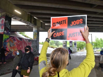A person holds a sign reading "CLIMATE, JOBS, CARE, JUSTICE" under an overpass